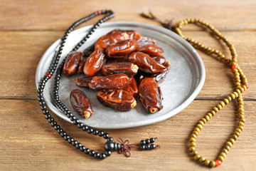 Composition of dried dates in holiday dish and rosary on wooden background