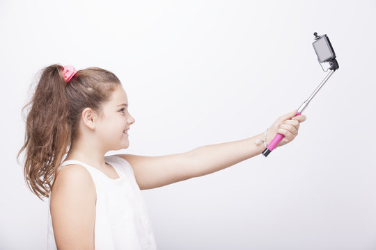 Little girl using a selfie stick on grey background