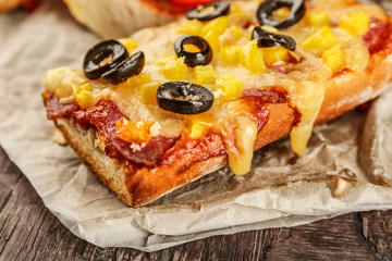 Hot pizza baguette with olives, paprika and salami on wooden table