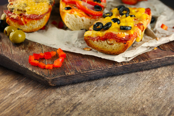Hot pizza baguettes with olives, salami, ham and cheese on wooden table