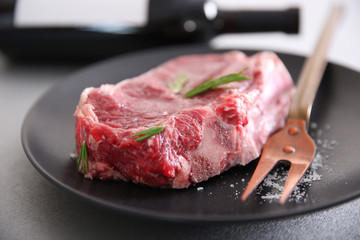 Raw pork steak with meat fork and rosemary on black plate