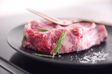 Raw pork steak with meat fork and rosemary on black plate