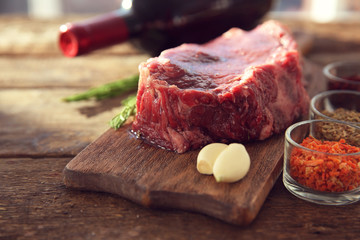 Raw pork steak with bottle of red wine and spices on wooden background