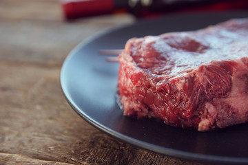 Raw pork steak with bottle of red wine on black plate