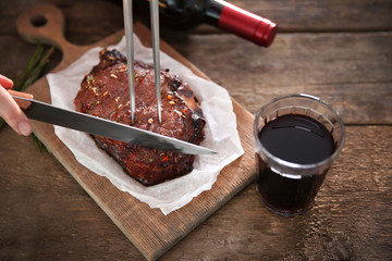 Roasted pork steak with wineglass, meat fork and knife on wooden background