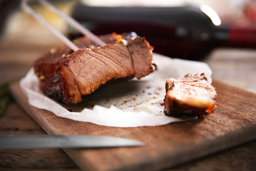 Sliced roasted pork steak with meat fork and knife on wooden background