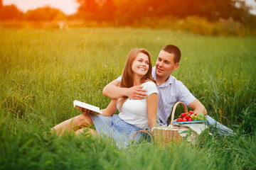 Young woman and man on the picnic in sunset meadow