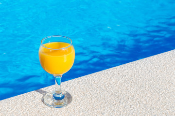 Glass with orange juice on edge of swimming pool
