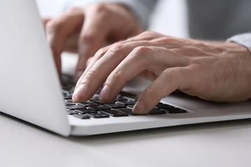 Male hands typing on laptop keyboard at table closeup