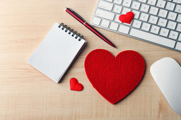 Computer peripherals with red hearts, pen and notebook on light wooden table