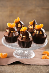 Tasty cupcakes with slice of mandarin and chocolate on wooden background