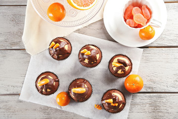 Tasty cupcakes with slice of mandarin and chocolate on a paper over light wooden background