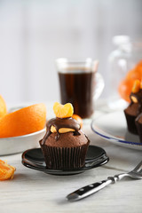 Tasty cupcake with slice of mandarin and chocolate on a plate over light wooden background