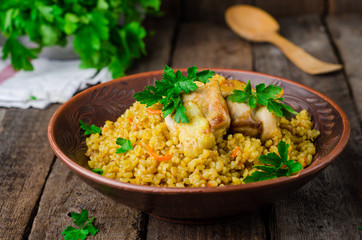 Chicken bulgur pilaf in clay bowl on wooden background. Selective focus