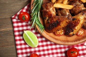 Baked chicken wings with French fries on brown plate
