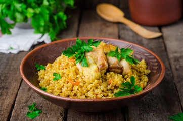 Chicken bulgur pilaf in clay bowl on wooden background. Selective focus