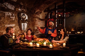Medieval people eat and drink in ancient castle kitchen interior.