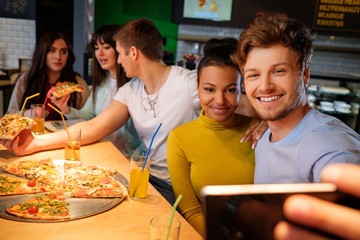 Cheerful multiracial friends taking selfie in pizzeria.