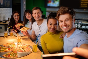 Cheerful multiracial friends taking selfie in pizzeria.