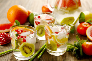 Refreshing cocktails with ice, pomegranate seeds and slices of fruits on wooden background