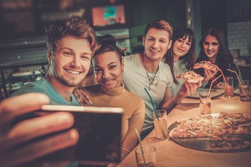 Cheerful multiracial friends having fun eating in pizzeria.