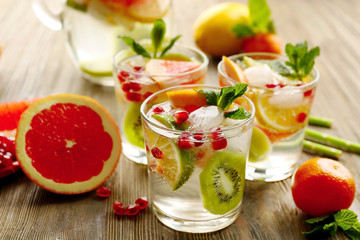 Refreshing cocktails with ice, mint, pomegranate seeds and slices of fruits on wooden background