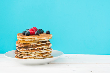 Pancakes with blueberries and raspberries on blue background
