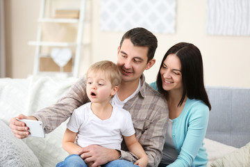 Fototapeta premium Happy family making selfie with mobile phone on couch, indoor