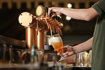 Mains de barman versant une bière blonde dans un verre.
