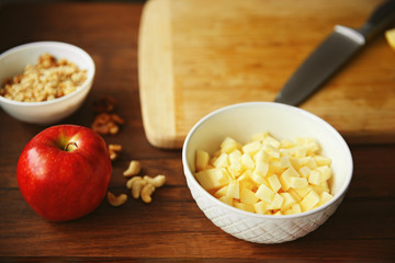 Chopped apples in bowl beside cutting board on wooden background