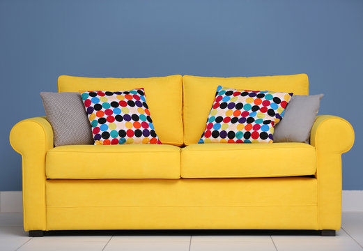 Yellow sofa and multicoloured pillows on a blue wall background