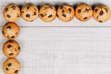 Homemade chocolate chip muffins as a frame on white wooden table.