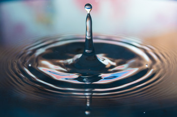 Macro photo of water drops falling into a pool of water, causing a splash and ripples.