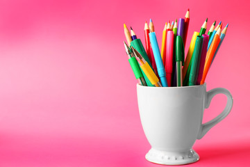Colorful stationery in white cup on pink background