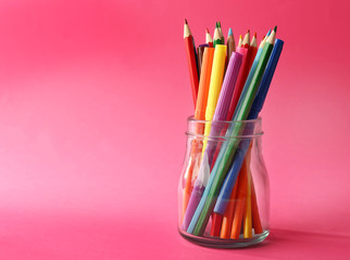 Colorful stationery in glass jar on pink background