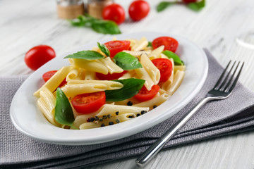 Plate of pasta with cherry tomatoes and basil leaves on table closeup