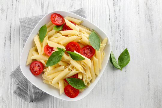 Plate of pasta with cherry tomatoes and basil leaves on wooden table, top view