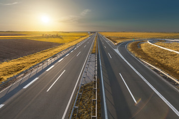 Open freeway through illuminated golden fields