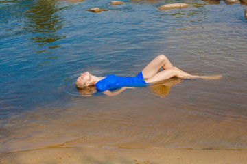 The beautiful blonde lies in the water in a dress