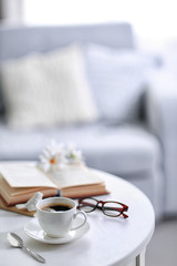 White cup of the coffee and a book on a table  in a light room..