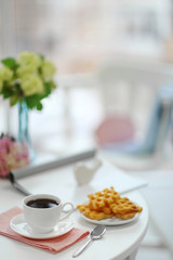 White cup of the coffee and sweets on wooden table  in a light room.