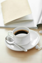 White cup of the coffee and a book on the table.
