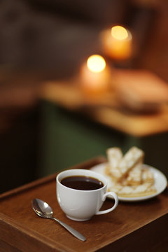 White cup of the coffee and biscuits on a wooden table in a dark room..