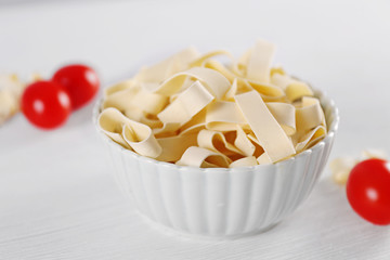 Bowl of uncooked pasta on wooden background