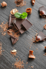 Pieces of chocolate with hazelnuts and fresh mint on black wooden background
