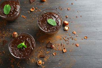 Glass cups of chocolate dessert with fresh mint and hazelnuts on black wooden table