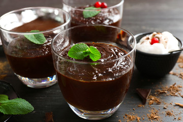 Glass cups of chocolate dessert with fresh mint and frothed milk on black wooden table
