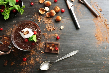 Glass cup of chocolate dessert with cranberries, fresh mint and frothed milk on black wooden table