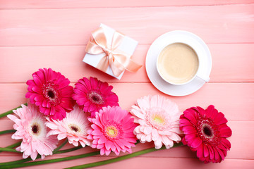 Bouquet of gerbers and present box on pink wooden ackground