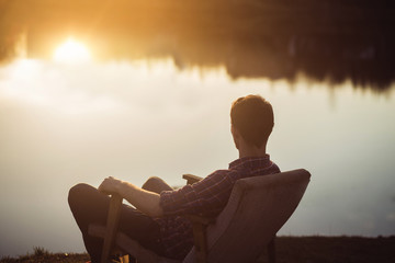 Man in the seat at bank of  lake also looks afar on sunset